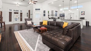A spacious living room with a large sectional sofa, a coffee table, and a dining area with a kitchen in the background. - Southtown Charm: Pool, Arcade & King Beds (San Antonio)