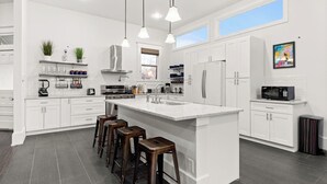 Une cuisine moderne avec des meubles blancs, un îlot central doté de tabourets, des appareils en acier inoxydable et un éclairage suspendu.
