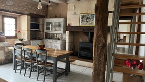 Eine rustikale Küche mit Holzofen, einem Essbereich mit Holztisch und -stühlen sowie einer Treppe mit hölzernem Geländer.