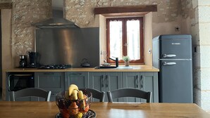 Eine Küche mit Steinwand, Gasherd, Wasserkocher, Kaffeemaschine, Kühlschrank und einem Esstisch mit Stühlen.