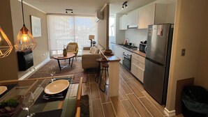 A modern kitchen with a refrigerator, stove, and dining area with chairs and a table. - Oceana Suites Bosque Pucalan (Puerto Montt)