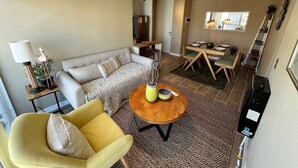 A living room with a sofa, a yellow armchair, a round wooden coffee table, and a dining area with a table and chairs. - Oceana Suites Bosque Pucalan (Puerto Montt)