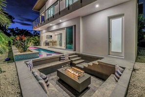 A modern outdoor living area with a pool, a fire pit, and a dining setup.