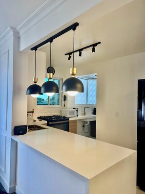 A modern kitchen with a white island, black pendant lights, and a view of the city through the window. - 3-bedroom apartment in terrific Rio de Janeiro LEBLON 200 mts from the beach-Ac (Rio de Janeiro)