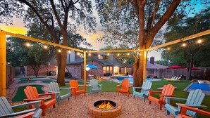 An outdoor patio area with Adirondack chairs, a fire pit, and string lights. - Heated Pool | MiniGolf |Arcade| Slide-Family Oasis (San Antonio)