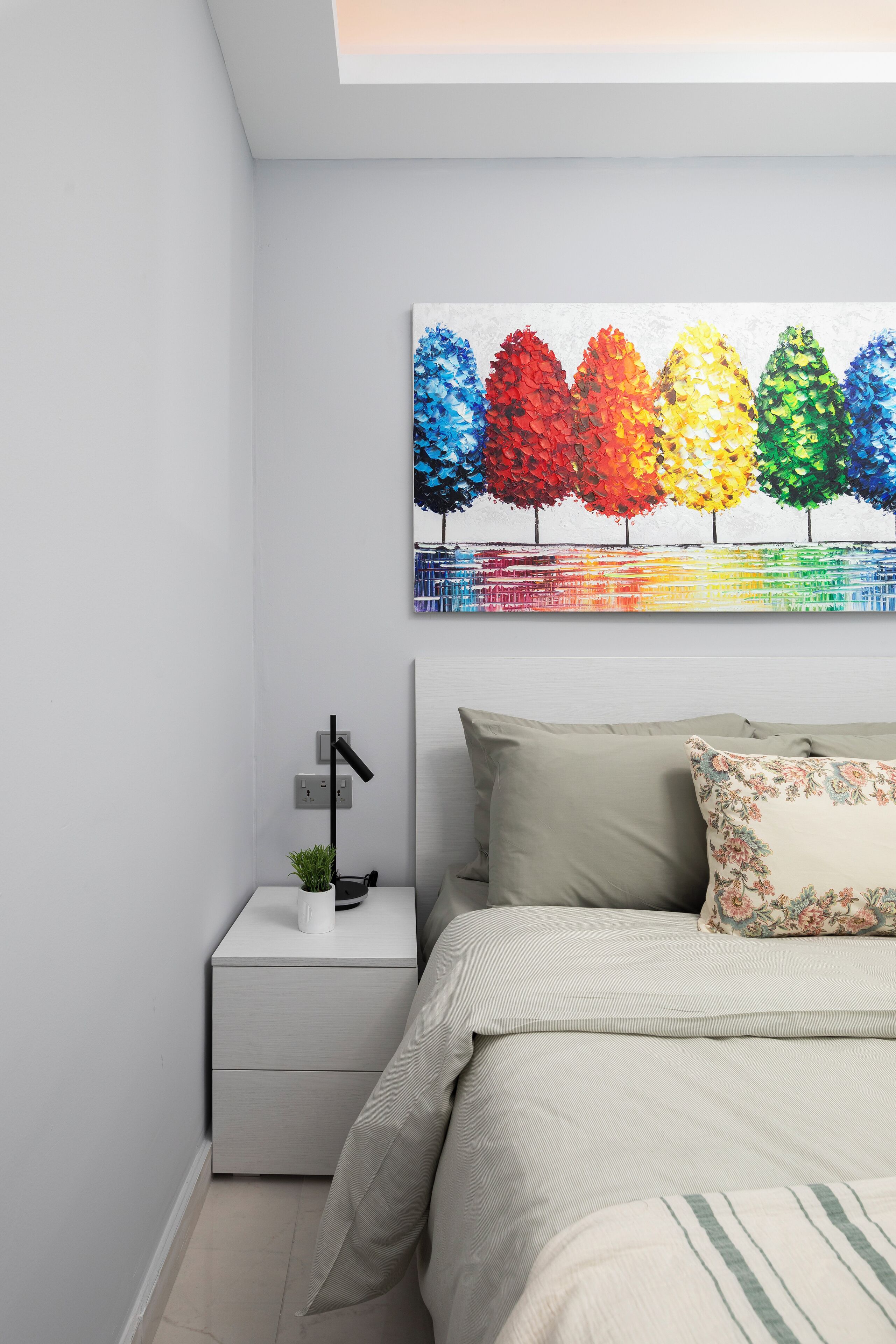 Una camera da letto con un letto, un comodino, una lampada e un quadro colorato sopra il letto.