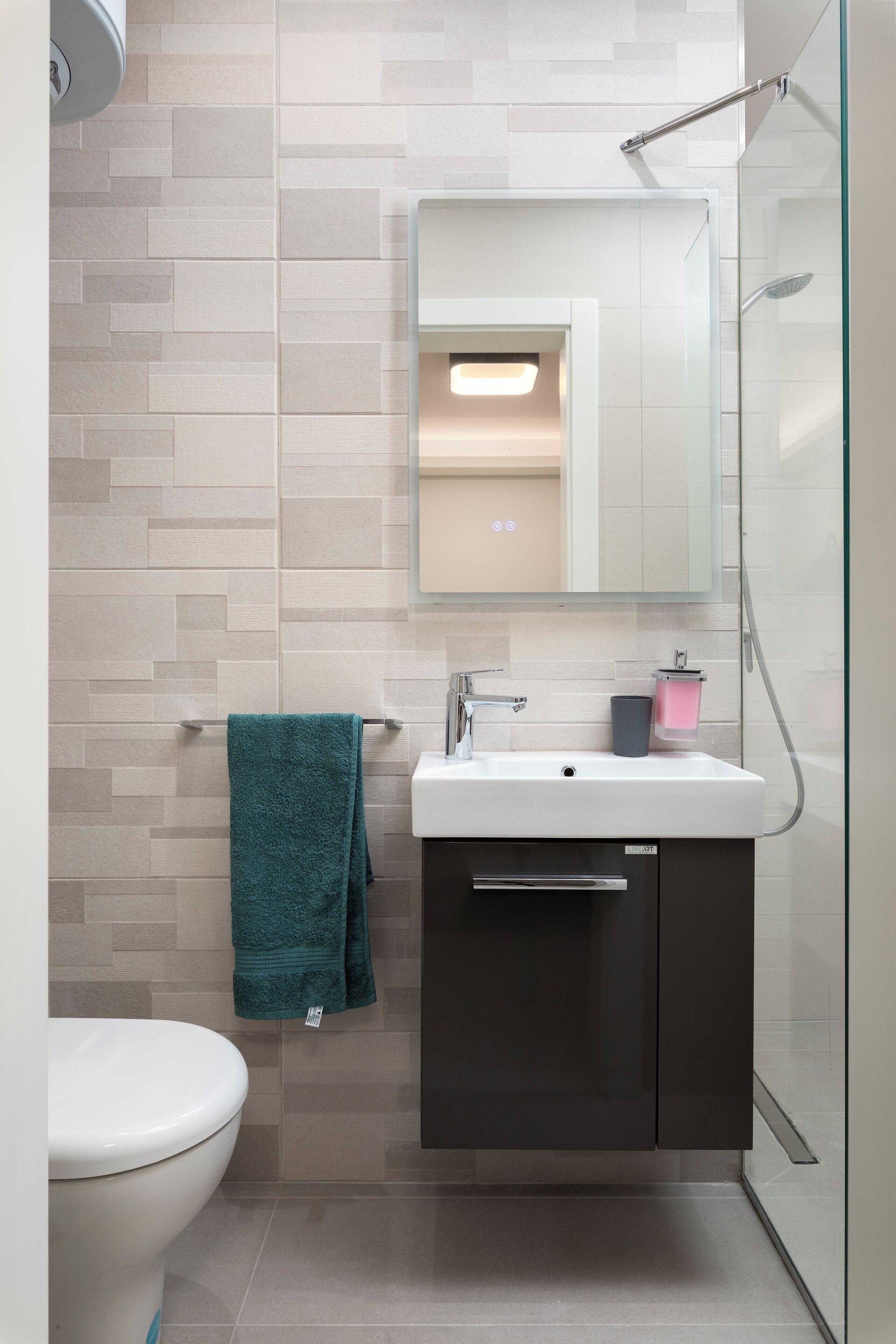 Ein modernes Badezimmer mit Toilette, Waschbecken und einem Spiegel darüber sowie einer Duschkabine aus Glas.