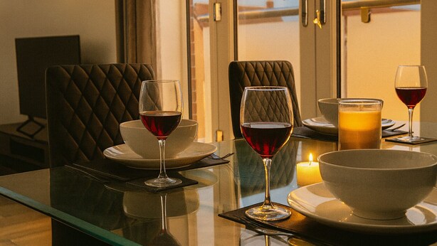A dining table with two wine glasses, a candle, and a glass of orange juice. - Modern 1BR | Sleeps 4 | Parking & Netflix (Weston Turville)