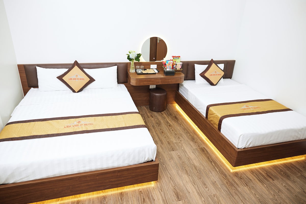 A hotel room with two beds, a wooden nightstand, and a mirror.