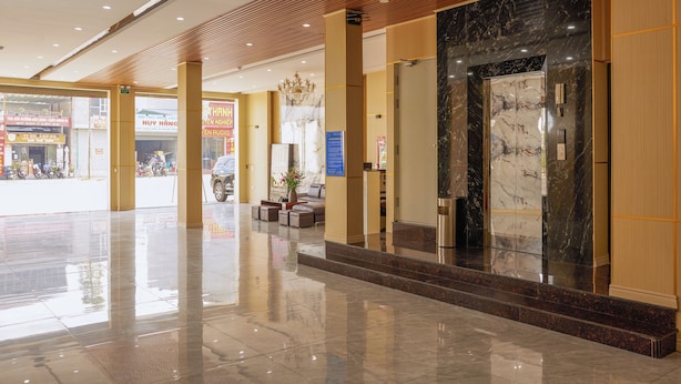 Et hotellobby med en marmorreception, en lysekrone og et siddeområde med en potteplante.