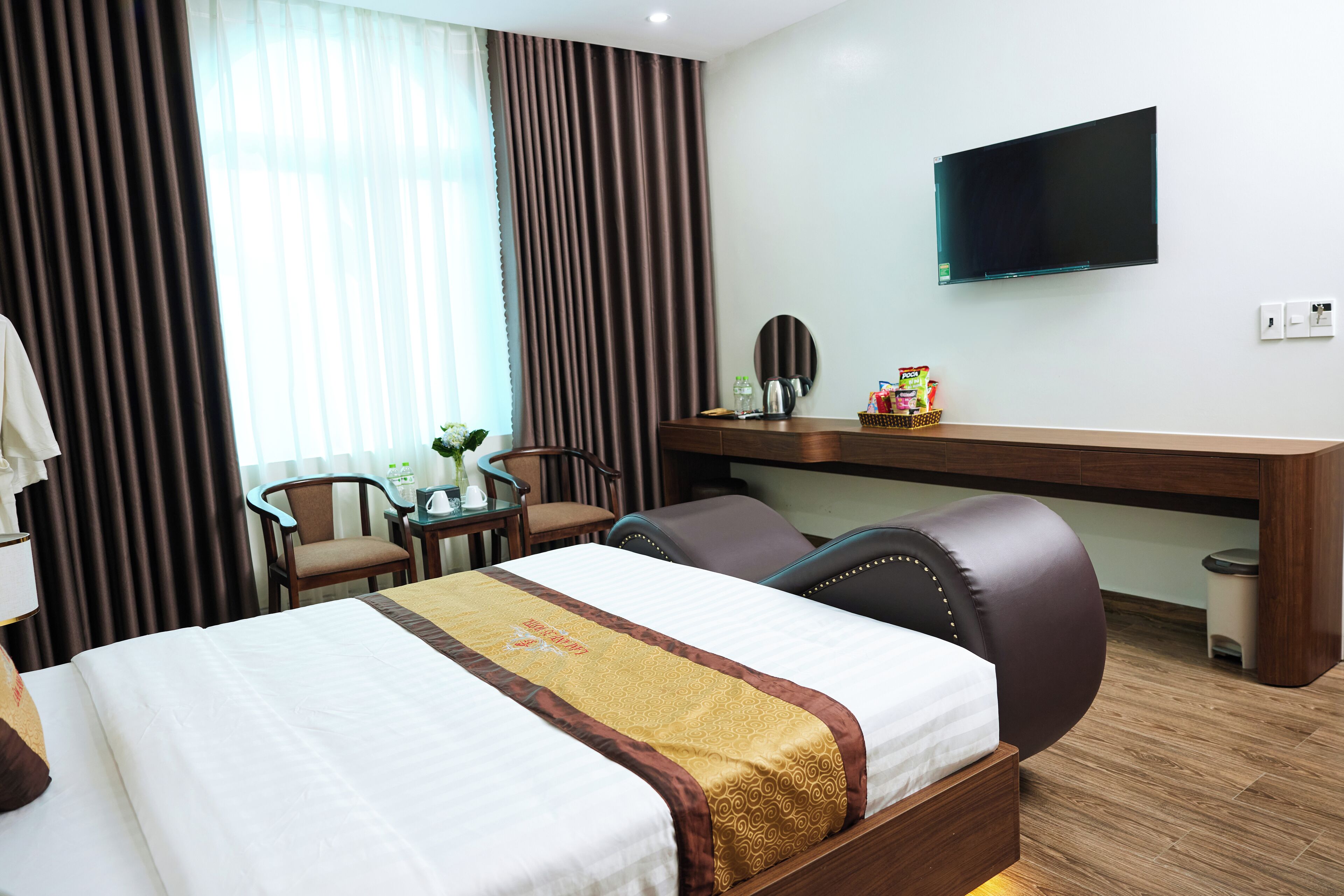 Una habitación de hotel con cama, escritorio, silla, televisor y ventana con cortinas.