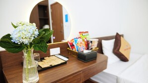 Et hotelværelse med et træskrivebord, en vase med blomster, et spejl, snacks og en seng med puder.