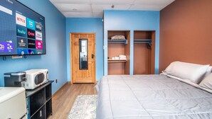A hotel room with a bed, a TV displaying various streaming services, a microwave, a refrigerator, and a wardrobe with shelves.