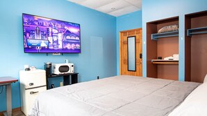 A bedroom with a bed, a television on the wall, a microwave, a small refrigerator, and a wooden door.