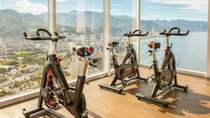 Three stationary bikes in a room with large windows overlooking a city and mountains. - Harbor Nt702 by Moikkarentals (Puerto Vallarta)
