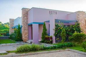 Un bâtiment moderne à la façade rose et aux éléments décoratifs en pierre, entouré d’un aménagement paysager soigné.