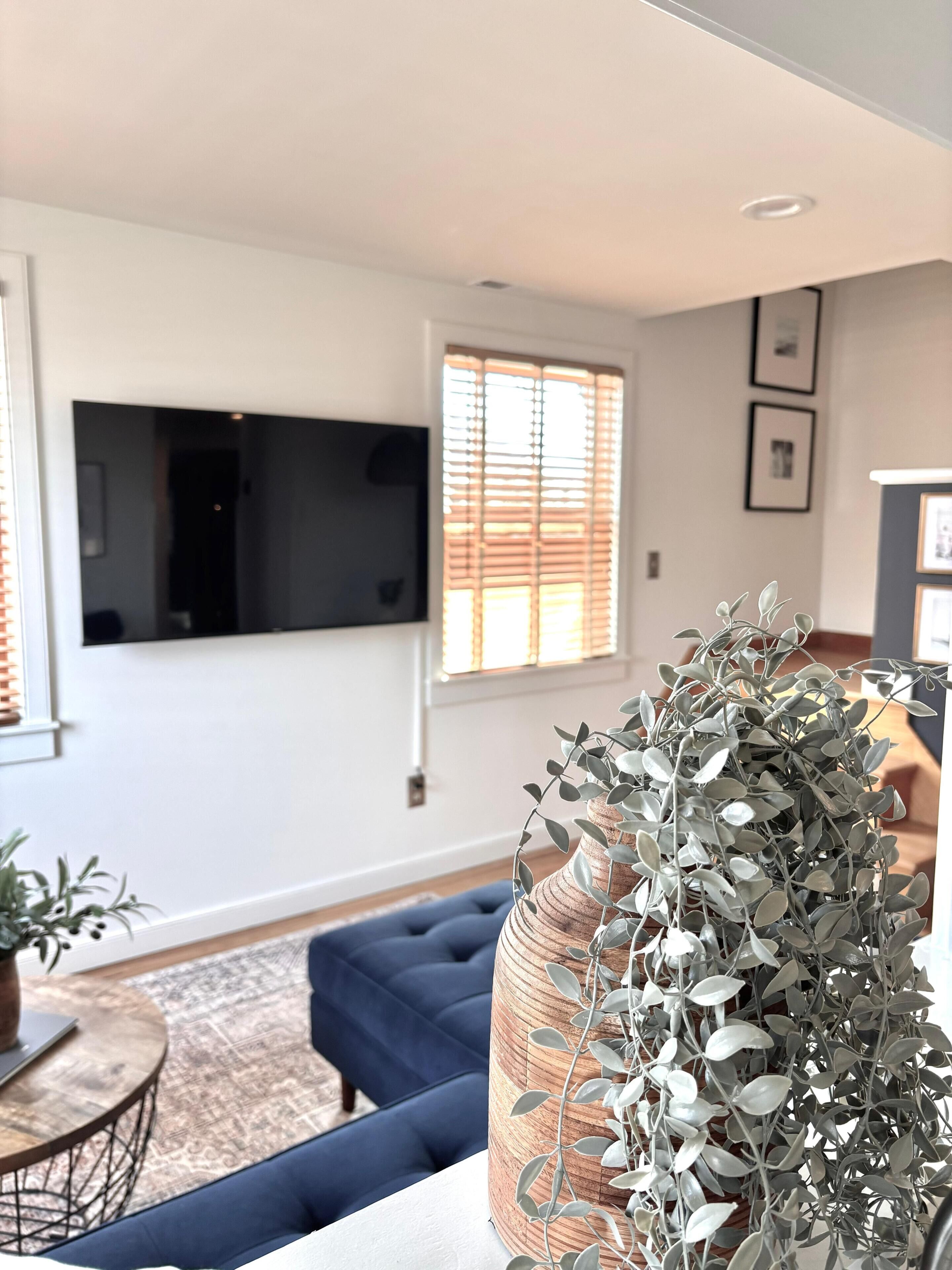 A living room with a sofa, a television mounted on the wall, and a window with blinds.