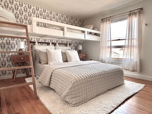 A bedroom with a bunk bed, a ladder, a bedside table, and a window with curtains. - Victorian Charm • Heart of Cape May • Rooftop Deck (Cape May)