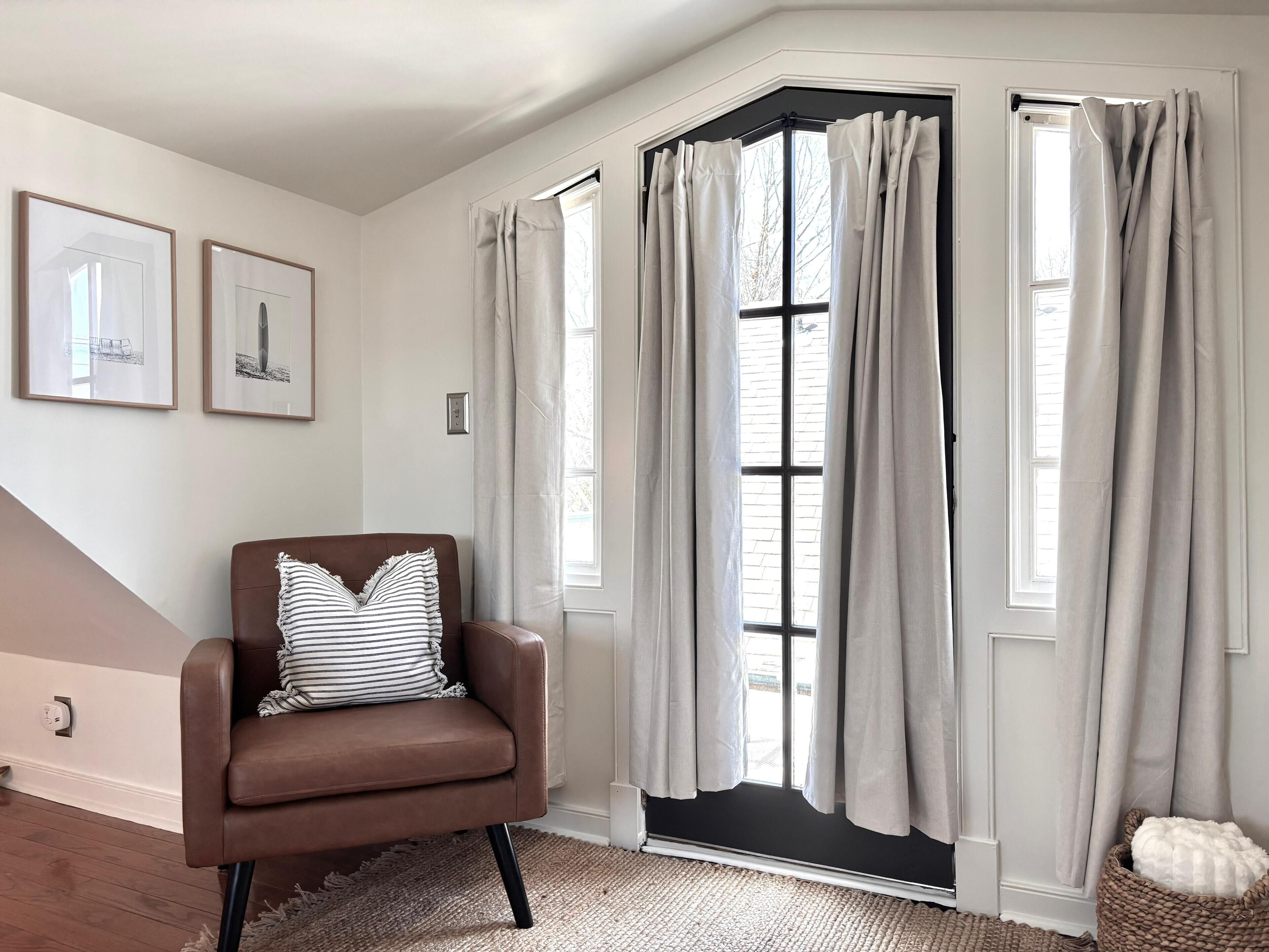 Une pièce d’angle avec un fauteuil en cuir marron, un tapis et une fenêtre avec des rideaux.