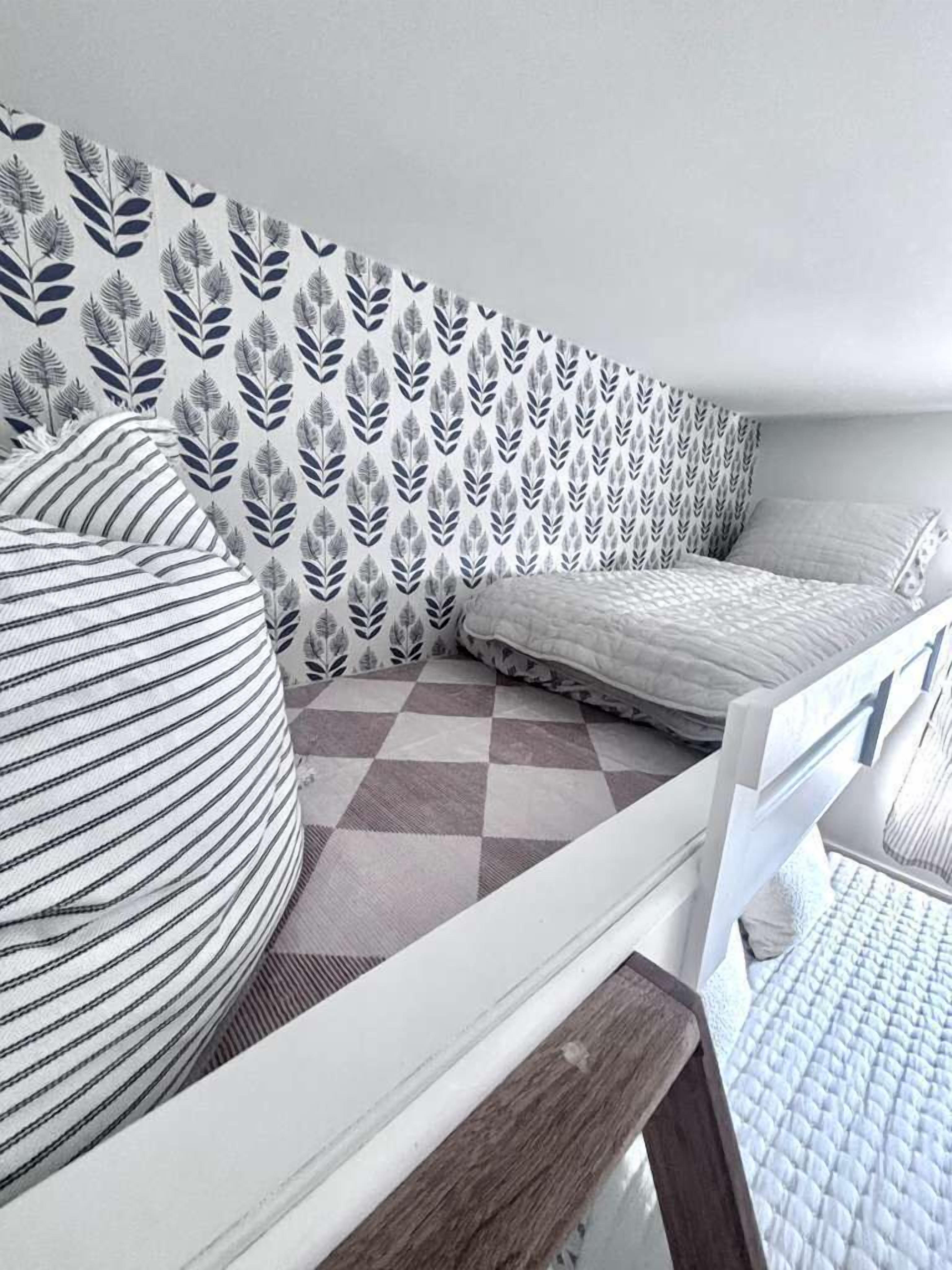 A bedroom with a checkered floor, a bed, a pillow, and a wall with a leaf pattern.