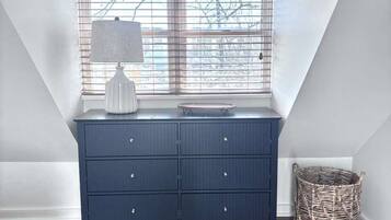 A bedroom with a large window, a dresser, a lamp, a rug, and a wicker basket.