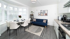Een moderne keuken met witte kasten, een blauwe bank en een eethoek met witte stoelen en een tafel.