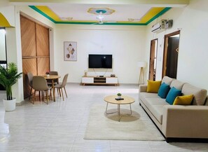 A living room with a sofa, a coffee table, a TV, and a dining area with chairs and a table. - Shivanya guest house (Varanasi)
