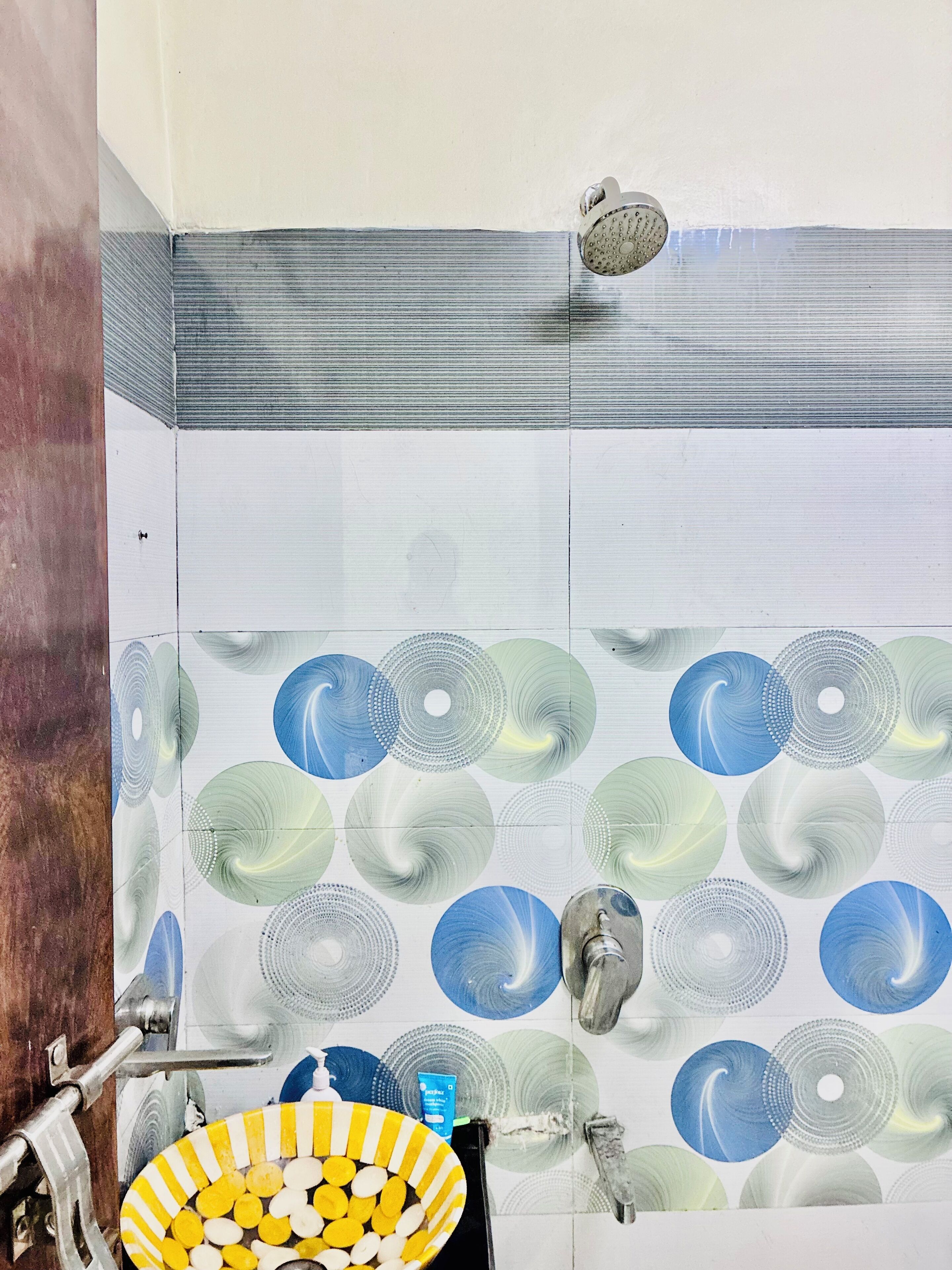 A bathroom with a patterned wall, a sink with yellow and white soap, and a shower with a silver head.