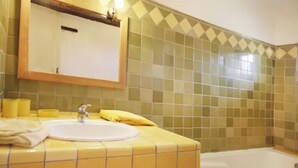 Een badkamer met een geel betegelde wastafel, een spiegel en een bad.