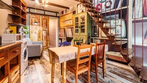 Un espace de vie compact comprenant un coin repas, un lave-linge, un canapé et un escalier décoré de vieilles valises.