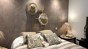 Ein Schlafzimmer mit einem Bett, zwei Kissen, einem Wandhaken für Hüte, einer Lampe und einem kleinen Tisch mit einem Hut.