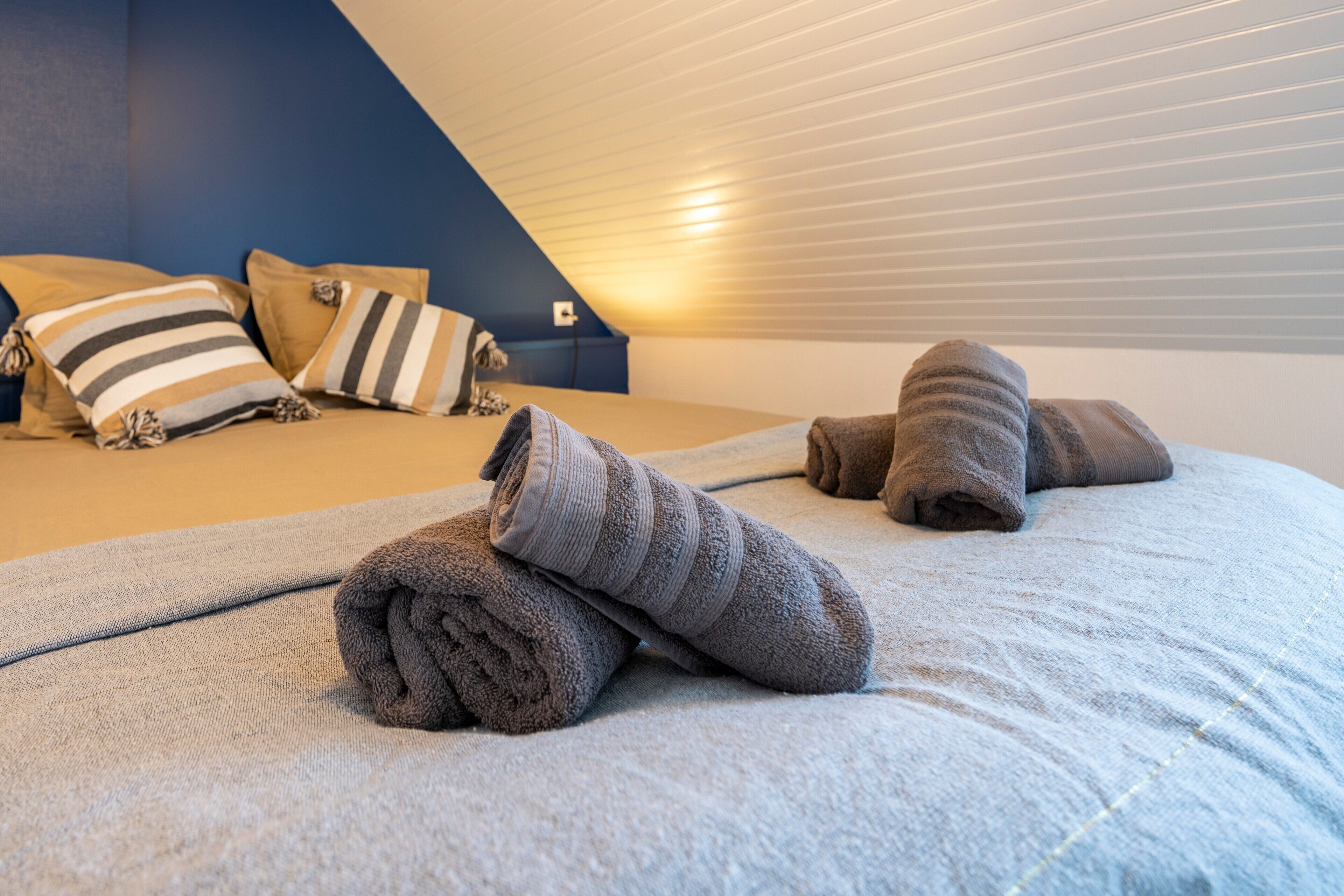 A bedroom with a bed, pillows, and rolled towels.
