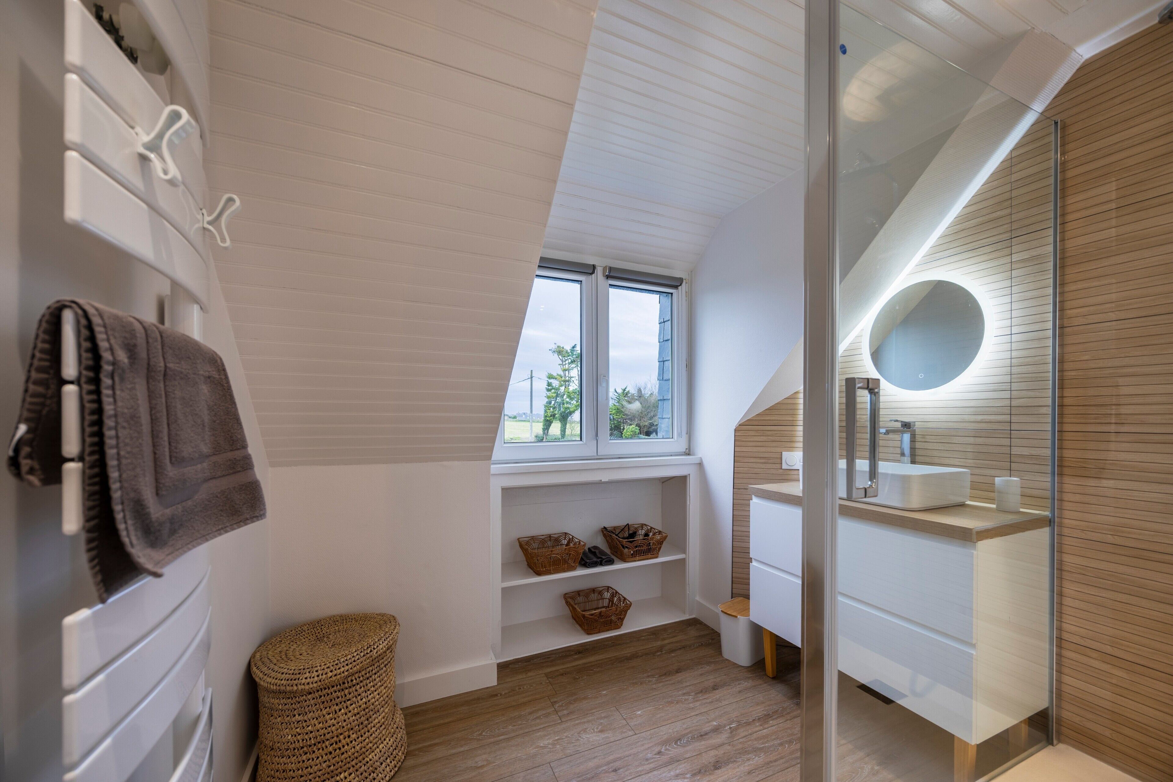 A modern bathroom with a skylight, built-in shelves, a vanity, and a round mirror.