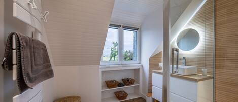 A modern bathroom with a skylight, built-in shelves, a vanity, and a round mirror.