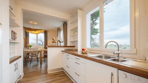 Een moderne keuken met houten vloer, witte kasten, een ingebouwde vaatwasser en een groot raam met uitzicht op de omgeving.