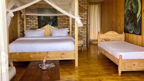 Ein Zimmer mit einem hölzernen Bett, einem zusätzlichen Bett, einem Holztisch und einem Bild an der Wand.