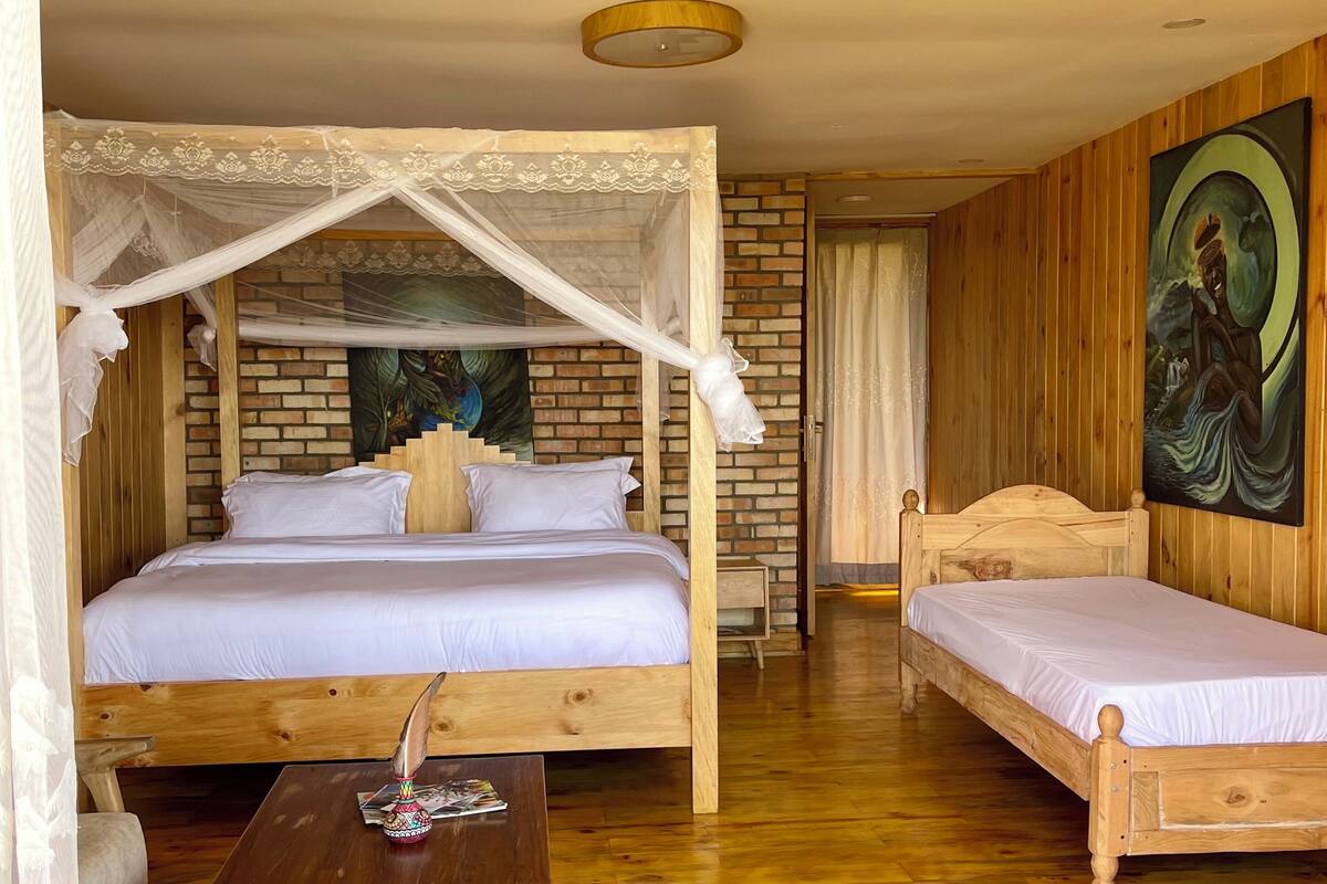 Una habitación con una cama de madera, una cama individual, una mesita de madera y un cuadro en la pared.