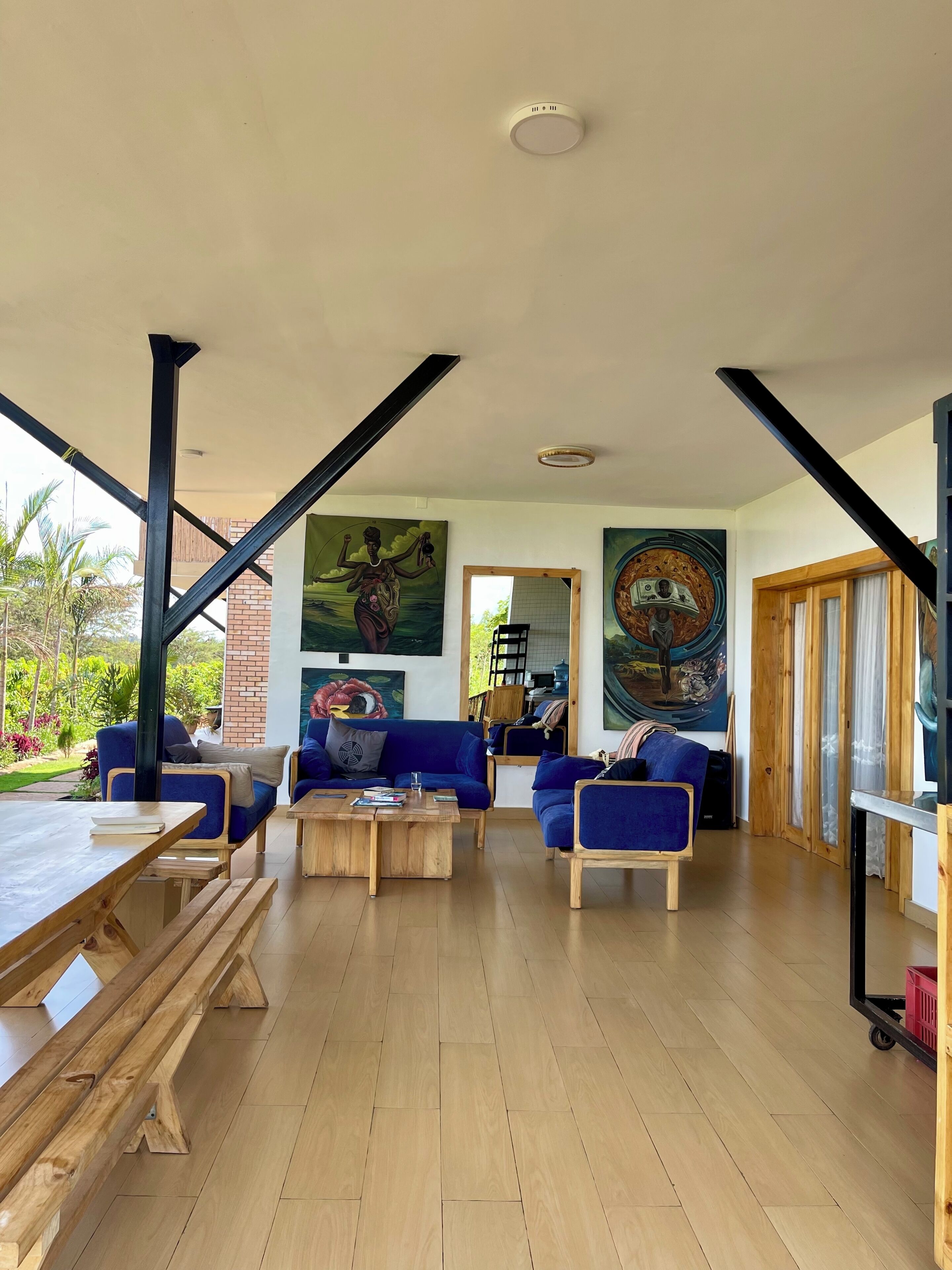 A spacious living area with a wooden floor, blue sofas, a wooden coffee table, and large paintings on the walls.