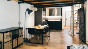 Una cocina moderna con vigas de madera, un comedor con una mesa dispuesta para dos personas y una escalera que sube a un nivel superior.