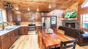 Ein Blockhaus-Interieur mit Holzwänden, einem Esstisch, einer Couch, einem Kamin und einem Fernseher.