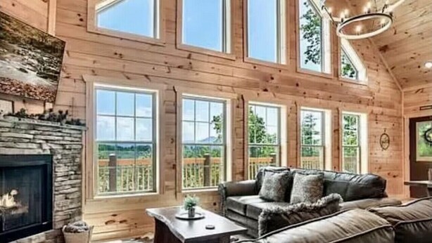 Ein geräumiges Wohnzimmer mit Kamin aus Stein, Ledersofa und großen Fenstern mit Blick ins Freie.