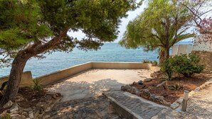A stone patio with a view of the sea, surrounded by trees and plants. - Seafront Chalet with Pool, Outdoor Kitchen, Spacious Garden and Stunning Views (Alicante (Alacant))