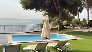A pool with lounge chairs and an umbrella, surrounded by a grassy area and trees. - Seafront Chalet with Pool, Outdoor Kitchen, Spacious Garden and Stunning Views (Alicante (Alacant))