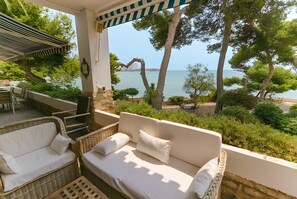 A balcony with a wicker sofa, a small table, and a chair. - Seafront Chalet with Pool, Outdoor Kitchen, Spacious Garden and Stunning Views (Alicante (Alacant))