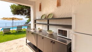 A kitchen with a view of a pool and chairs, a microwave, and a refrigerator. - Seafront Chalet with Pool, Outdoor Kitchen, Spacious Garden and Stunning Views (Alicante (Alacant))
