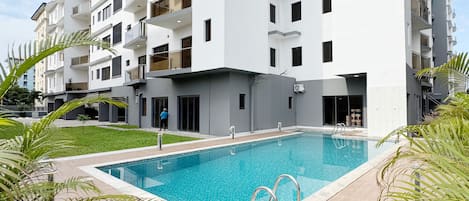 A modern multi-story residential building with a swimming pool in the foreground.