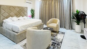 A modern bedroom with a large bed, a sofa, a coffee table, and a fan. - Luxury StudioApt•24/7Power•WiFi•Pool• Gym•Secured (Lekki)