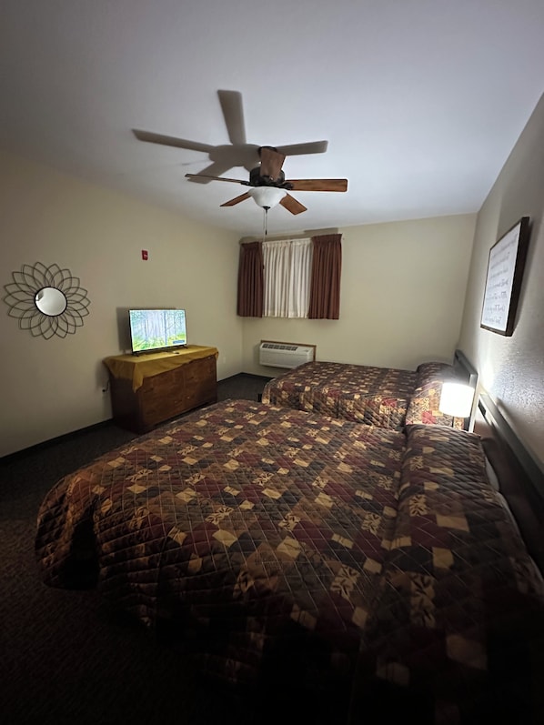 Quarto com cama, ventoinha no teto, televisão e cômoda.