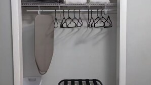 Um closet espaçoso com arara de metal, roupas penduradas e um banco.