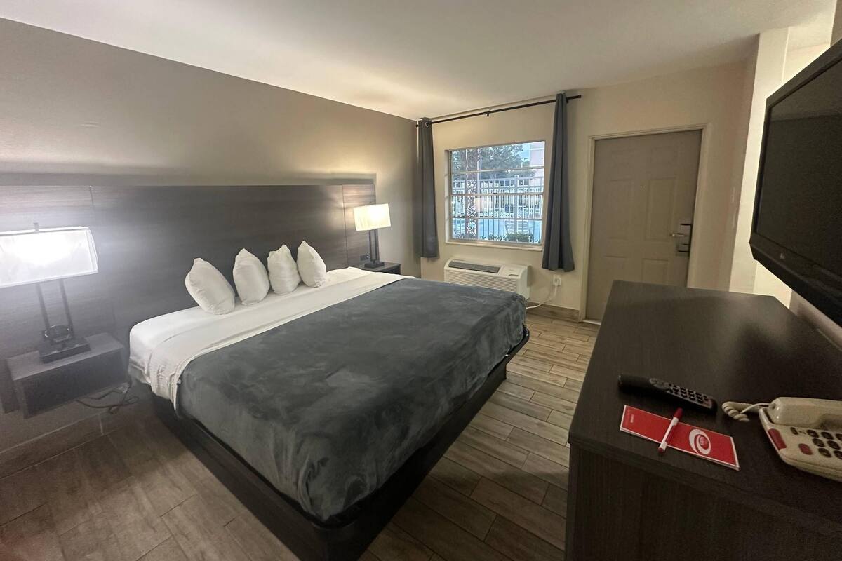 Et hotelværelse med seng, sengeborde, lamper, et TV, et skrivebord med telefon og et vindue med udsigt.